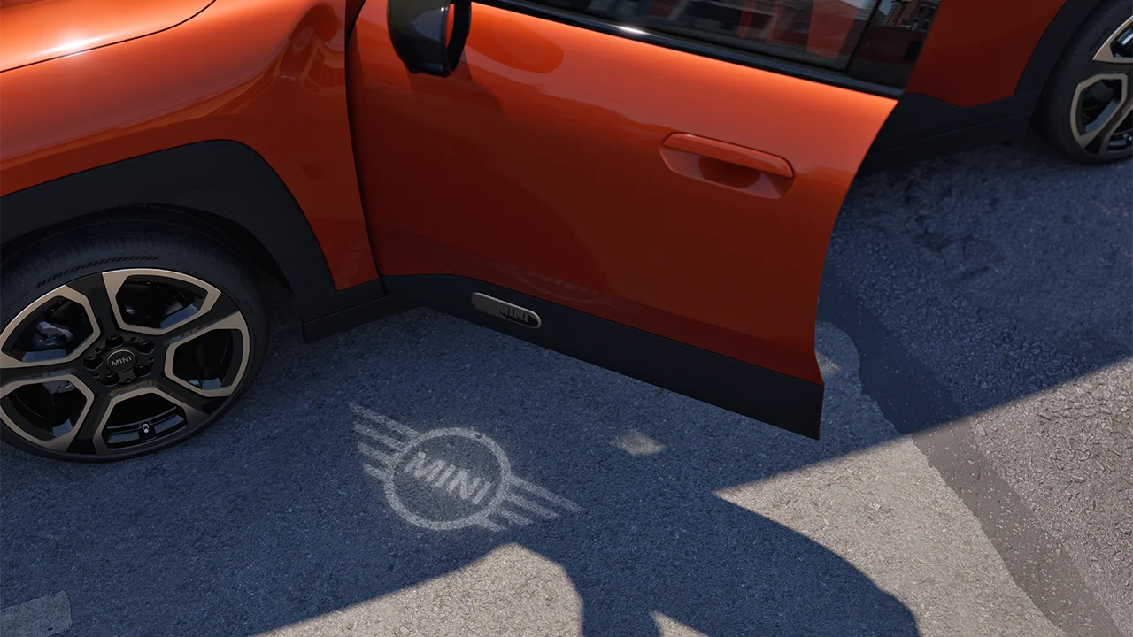 Vista externa do MINI Aceman totalmente elétrico com porta aberta e luz de boas-vindas com o logotipo da MINI no chão. 