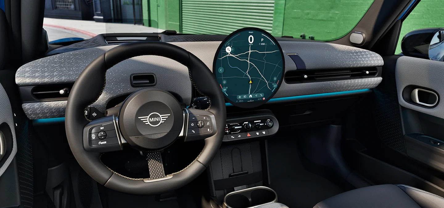 Vista interna do MINI Cooper 5 portas com foco no volante, no painel de instrumentos e na unidade de interação.