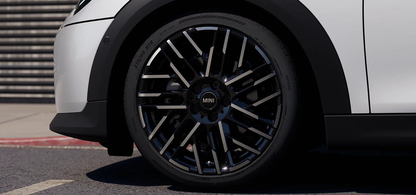 Imagem em close-up do MINI Cooper 5 portas na cor Nanuq White com rodas bicolores Night Flash Spoke.