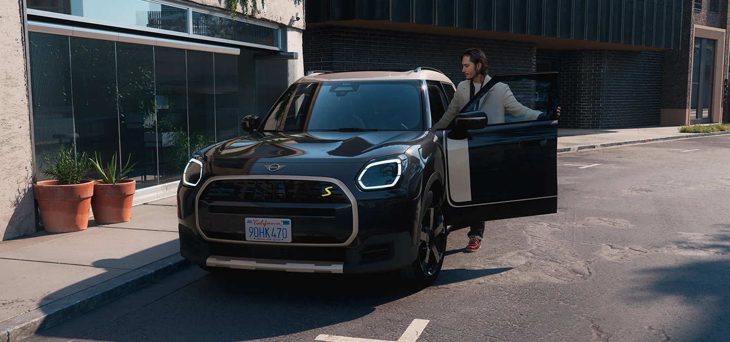 Vista frontal do MINI Countryman totalmente elétrico em Midnight Black e Vibrant Silver Roof, em uma rua.