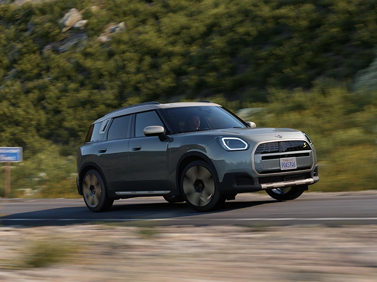 Vista lateral do MINI Countryman totalmente elétrico em movimento, na cor Smokey Green com teto Vibrant Silver, em um trecho offroad.