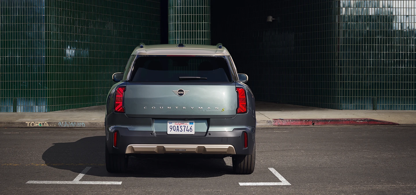 Vista traseira do MINI Countryman totalmente elétrico na cor Smokey Green com teto Vibrant Silver, estacionado. 