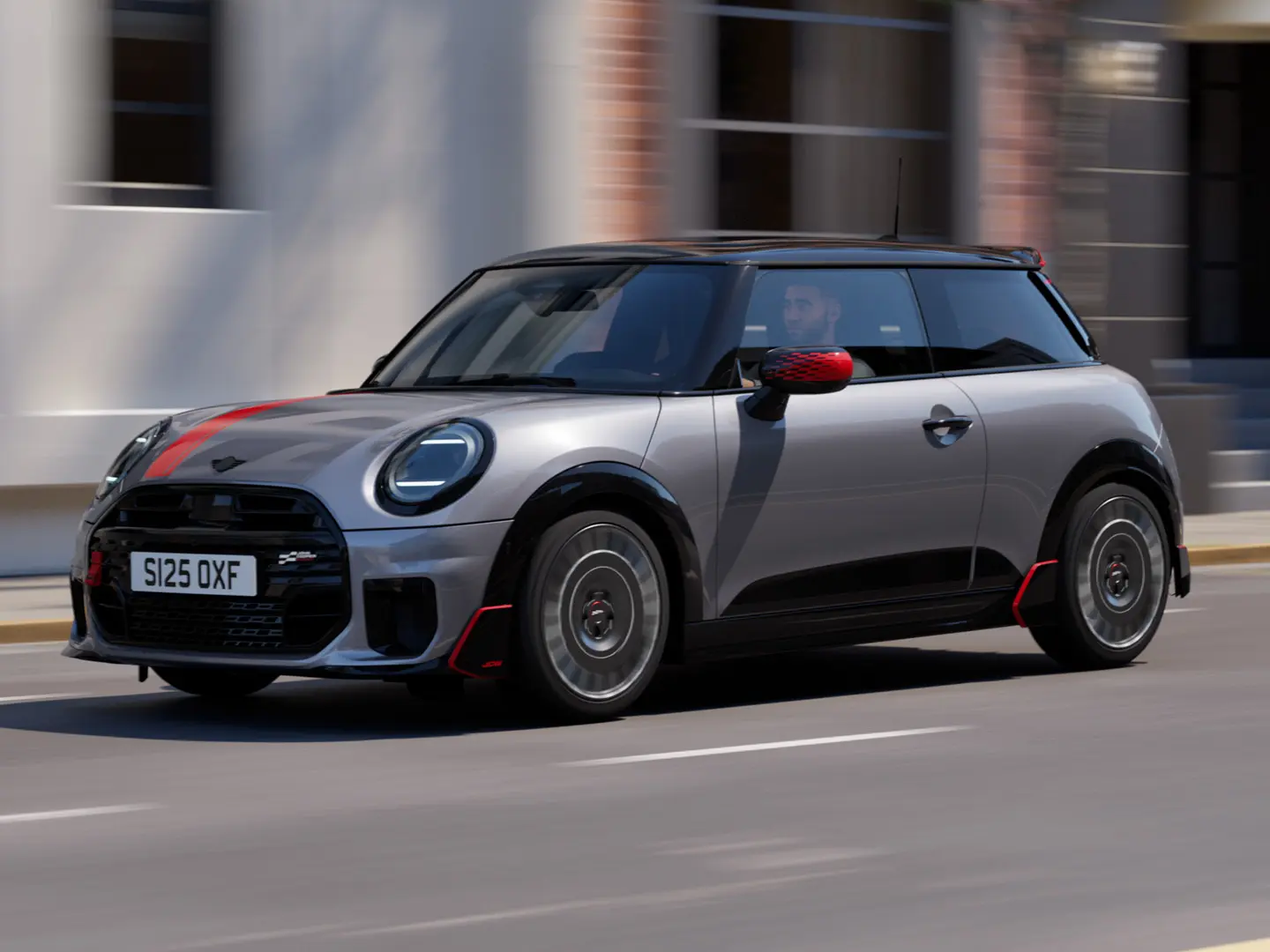 MINI Cooper 3 portas na cor Melting Silver com capas dos retrovisores John Cooper Works e adesivo para capô em Chili Red, spoiler de teto e winglet em Black, circulando por uma rua da cidade - vista frontal lateral.