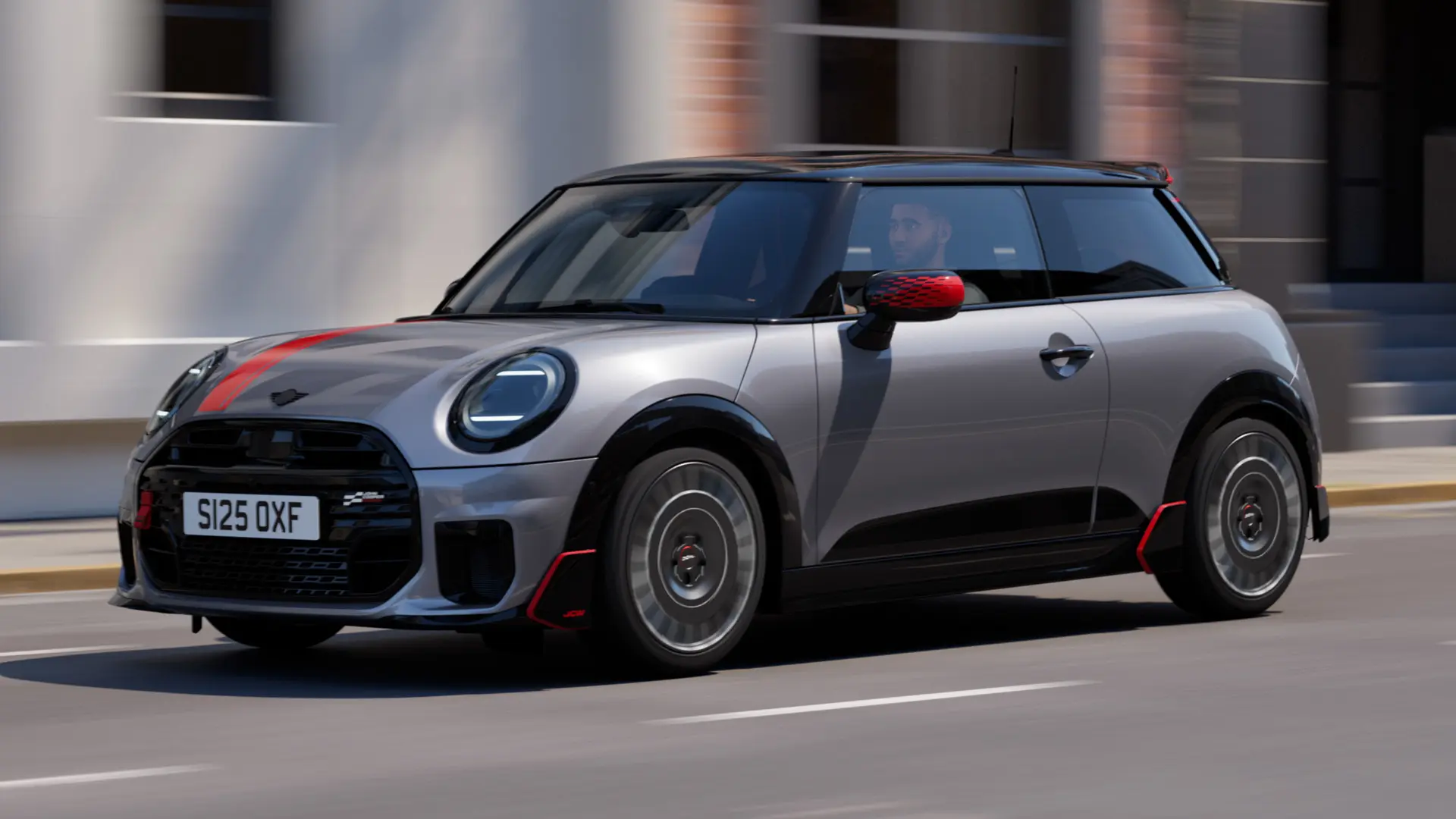 MINI Cooper 3 portas na cor Melting Silver com capas dos retrovisores John Cooper Works e adesivo para capô em Chili Red, spoiler de teto e winglet em Black, circulando por uma rua da cidade - vista frontal lateral.